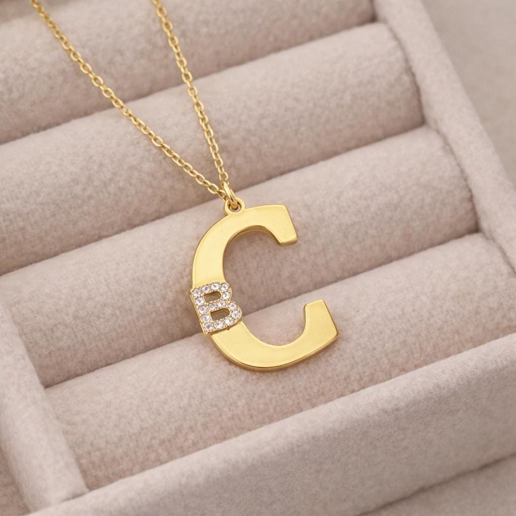 Close up gold letter necklace displayed on soft beige jewelry tray background