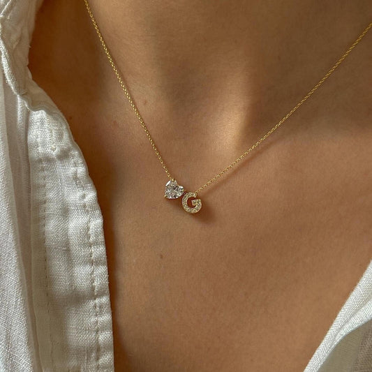 Dainty Diamond CZ Heart Initial Necklace. This stunning custom jewelry piece features 14K gold-plated 925 sterling silver with a sparkling heart-shaped cubic zirconia CZ stone, delicately set between two diamond-encrusted initial letters A-Z.