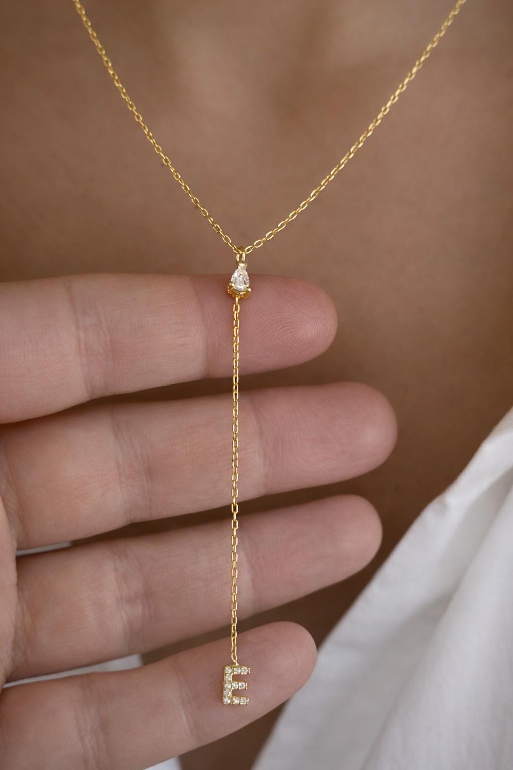 Gold lariat initial necklace with letter E pendant, dainty personalized drop necklace shown on hand with cubic zirconia stone detail