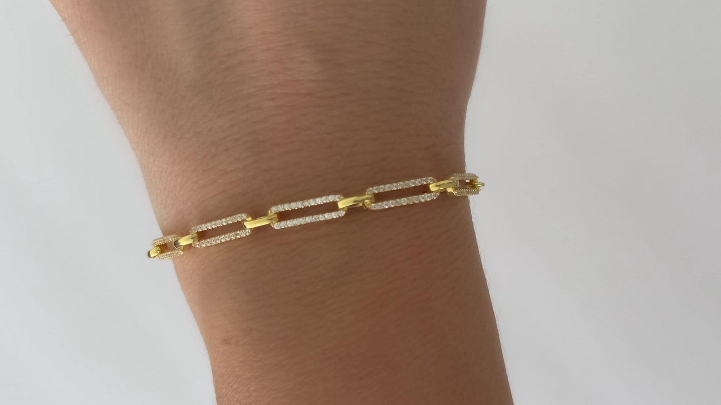May include: A gold chain bracelet with small square links. Each link is encrusted with small clear stones.