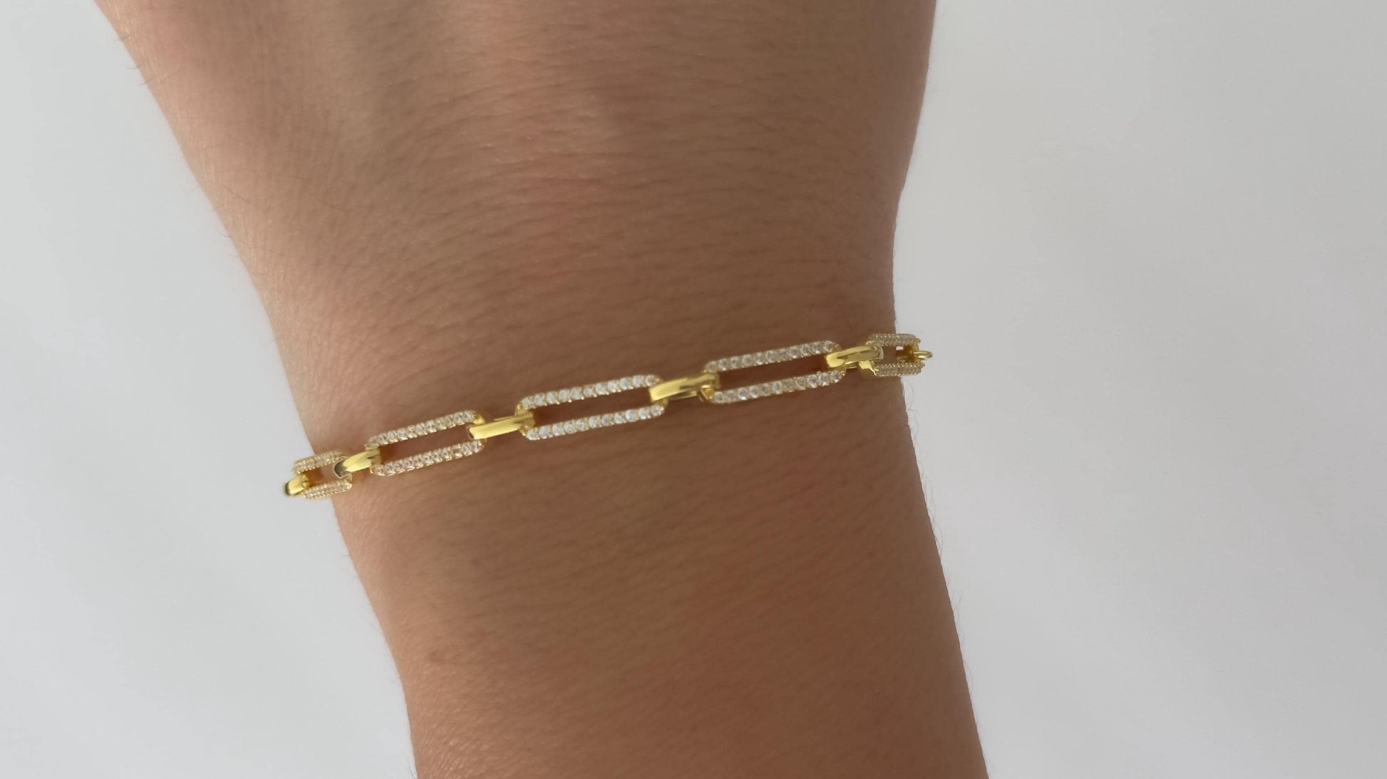 May include: A gold chain bracelet with small square links. Each link is encrusted with small clear stones.