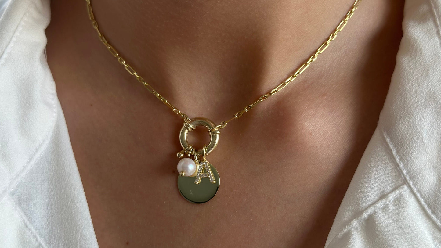 May include: A gold chain necklace with a round charm featuring a pearl and the letter "A".