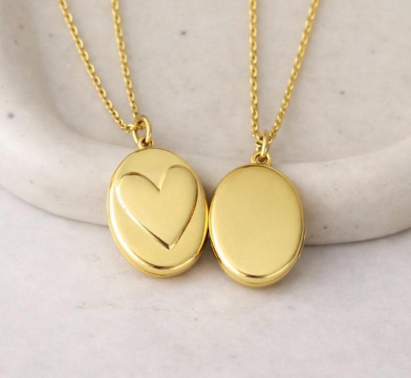 Gold photo locket necklace with heart and oval design on marble background