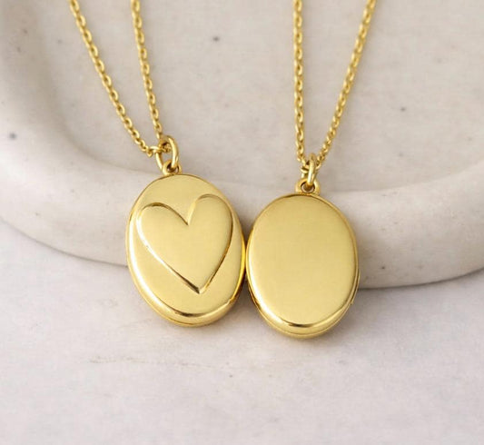 Gold photo locket necklace with heart and oval design on marble background