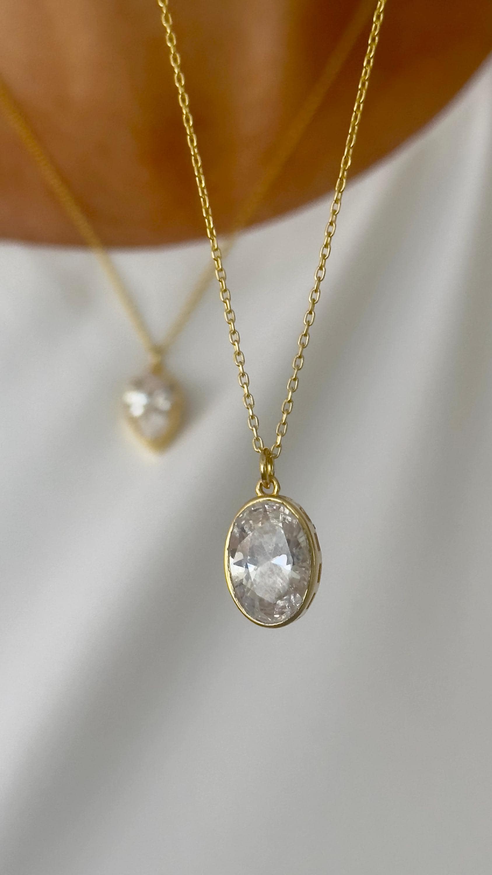 Close-up of oval-cut CZ gemstone necklace with gold bezel setting, dainty handmade jewelry for women.