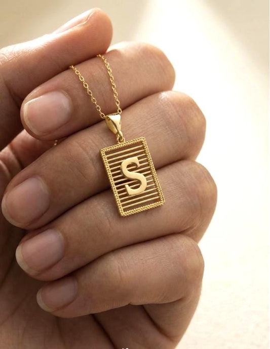 Gold initial necklace with 3D raised letter pendants on textured rectangular charms displayed on neutral background