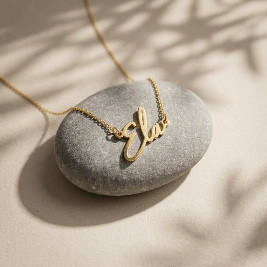 Gold script name necklace flat lay on stone background, dainty personalized necklace in minimalist style