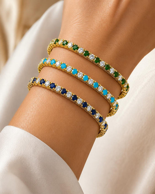 Woman wearing stacked 18K gold filled tennis bracelets featuring emerald, turquoise and sapphire gemstones with sparkling diamond accents. Waterproof stackable bracelet jewelry, tarnish resistant gift for her.