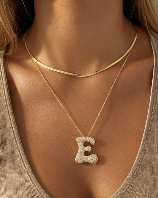 Jumbo bubble letter E necklace in gold finish with pavé CZ stones, oversized initial pendant necklace styled on model.