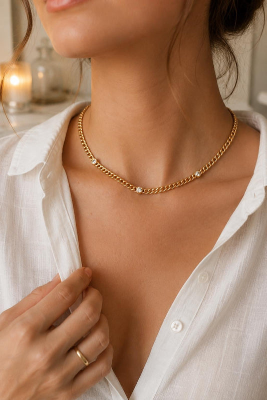 Woman wearing a gold triple CZ Cuban link choker necklace with three bezel-set cubic zirconia stones, styled with a white button-down shirt.