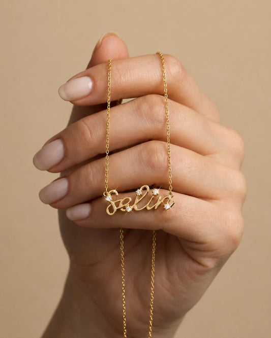Gold personalized script name necklace with clear diamond accents held in a woman’s hand, dainty custom name jewelry gift for her.