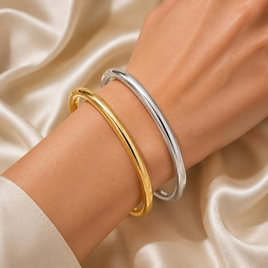Gold and silver thick round bangle bracelets worn together on a woman’s wrist, featuring a polished minimalist design for stacking.
