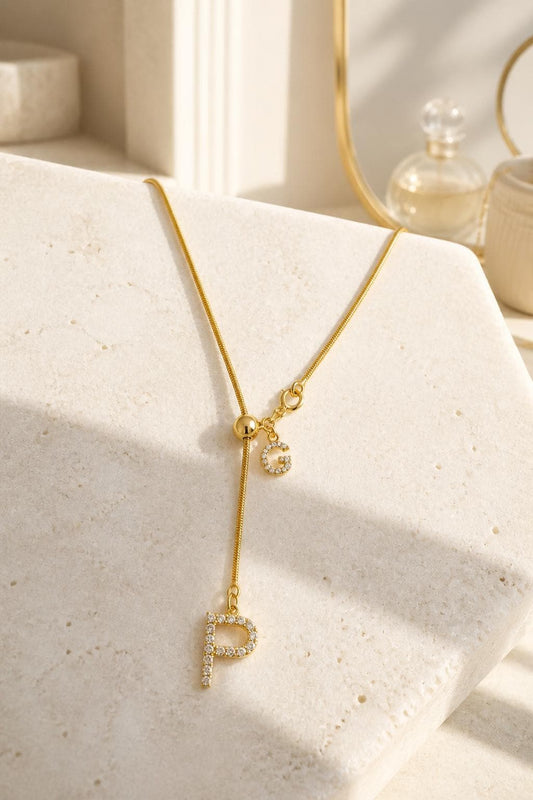 Personalized diamond initial lariat necklace with two letter charms, adjustable Y drop chain and sparkling gold finish displayed on a neutral stone surface.