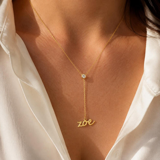 Dinaty gold drop name necklace with a clear bezel crystal and personalized Zoe script pendant, worn as an anniversary gift for her.